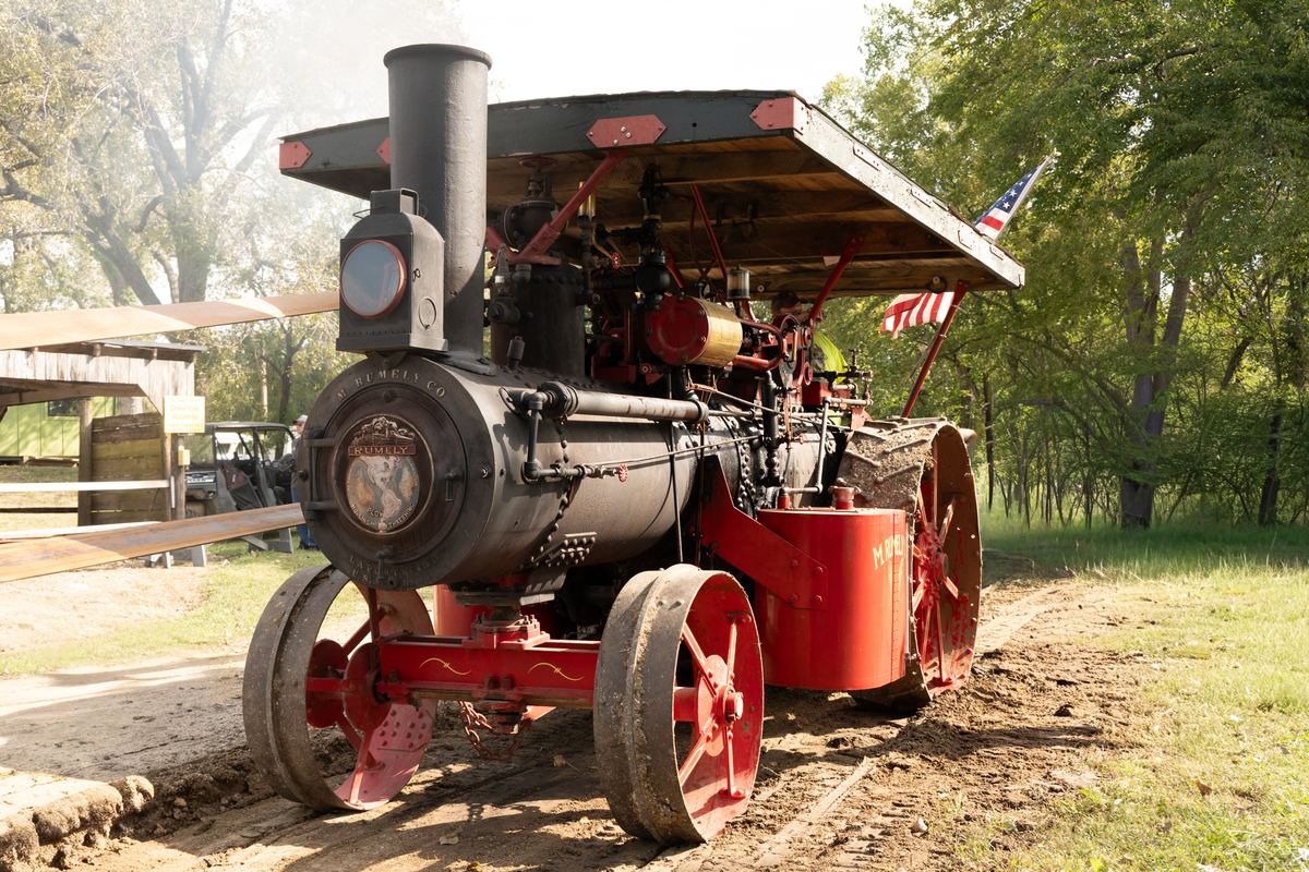 A restored red and black Rumely steam traction engine with smoke rising at a heritage threshing show
